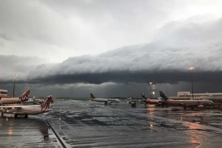 Aircraft grounded at Sydney Airport during severe storm with strong winds and dark clouds
